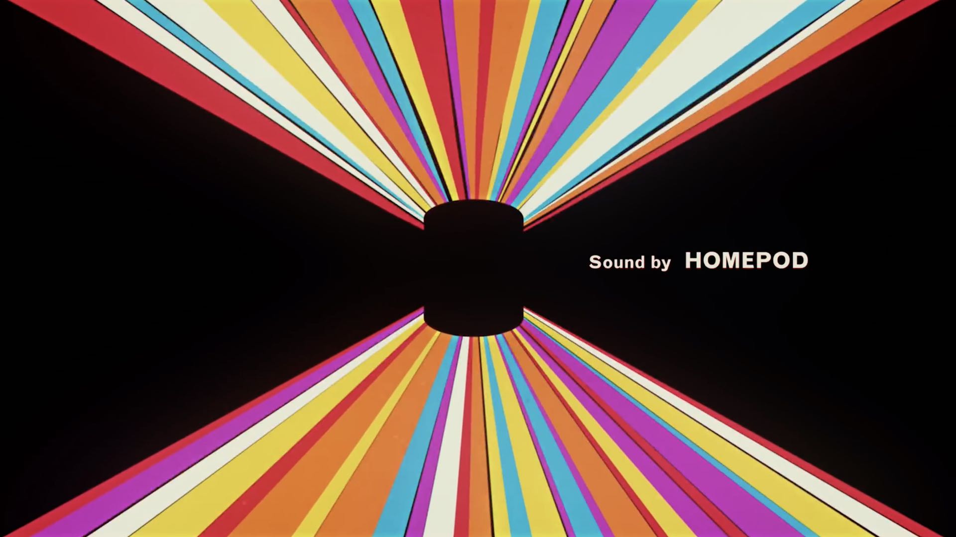 Un'immagine tratta dal video introduttivo di HomePod di Apple, che mostra lo smart speaker su uno sfondo nero con striature luminose colorate e lo slogan "Suono di HomePod"